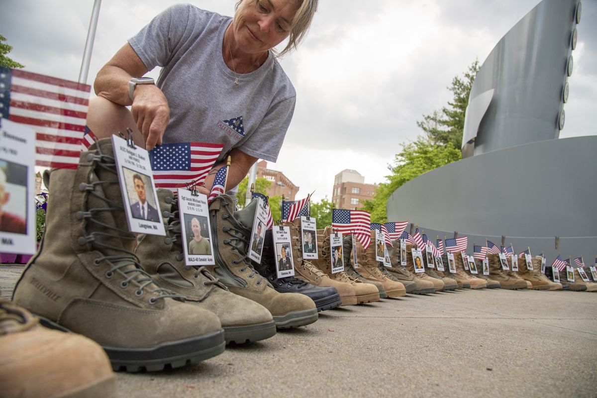 Gold Star mother Keirsten Lyons bends down near a military boot with a photo of her son, Sgt. Jacob Michael Hess, a Marine who was killed in 2014 in Afghanistan, at a display set up around the Illuminating Courage memorial outside the Spokane Veterans Arena on Saturday.  (Jesse Tinsley/THE SPOKESMAN-REVIEW)