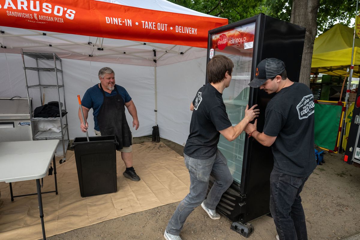 Caruso’s Sandwiches’ Brystol Myers, left, supervises the placement of a cooler being moved by employees Logan Pleger, center, and Keisyn Claunch as they set up their Pig Out In the Park food booth Tuesday in Riverfront Park.  (COLIN MULVANY/THE SPOKESMAN-REVI)