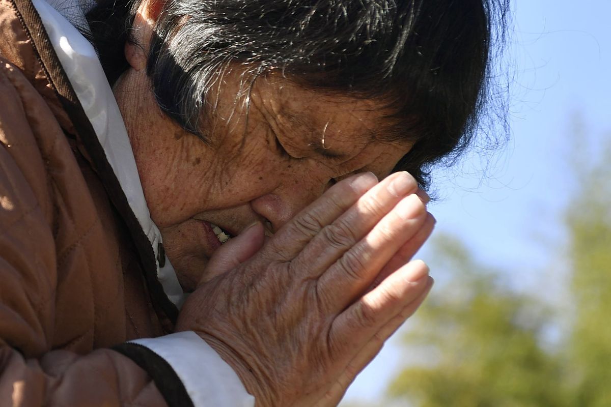 A woman who lost her husband and grandchild in the 2011 earthquake and tsunami, prays in front of the grave in Miyako, Iwate prefecture, Japan Thursday, March 11, 2021. Thursday marks the 10th anniversary of the massive earthquake, tsunami and nuclear disaster that struck Japan’s northeastern coast.  (Muneyuki Tomari)