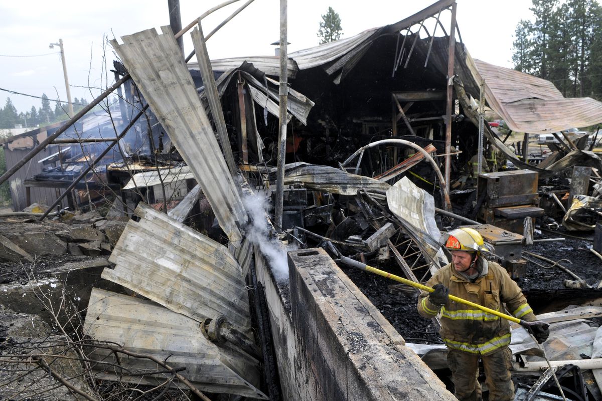 Spokane County District 3 firefighter Brad Kane pokes around at the smoldering foundation of the Spiral and Rail House on Geiger Boulevard after an early morning fire Wednesday destroyed the business. (Dan Pelle)