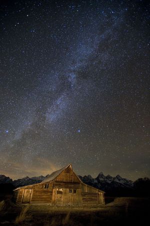 In this Thursday, Nov. 19, 2009 photo, the Milky Way spreads across the night sky over Mormon Row, an historic settlement, in Grand Teton National Park near Jackson, Wyo. The light in the distance is the city of Driggs, Idaho, on the west side of the Teton Mountain Range. (Bradly Boner / Jackson Hole News&guide)