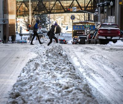Pedestrians make their way over a snow berm plowed in the middle of a street at Riverside Avenue and Lincoln Street, Jan 11, 2017, in downtown Spokane, Wash. (Dan Pelle / The Spokesman-Review)