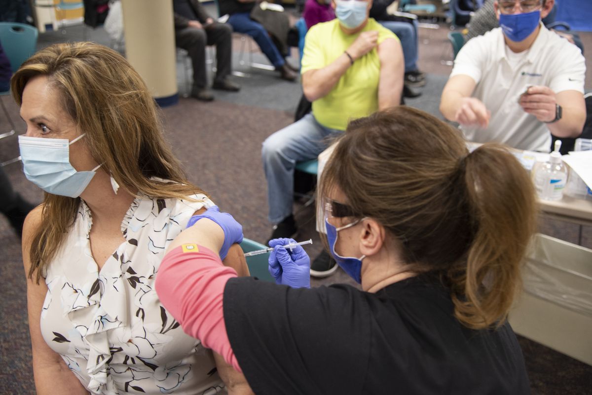 Robin Toth receives the Moderna COVID-19 vaccine from nurse Dawn Doud Friday at a pop-up clinic at Holy Family Hospital in north Spokane. Behind them, Michael Toth, Robin’s husband, prepares to get his dose from nurse Brian Baker.  (Jesse Tinsley/The Spokesman-Review)