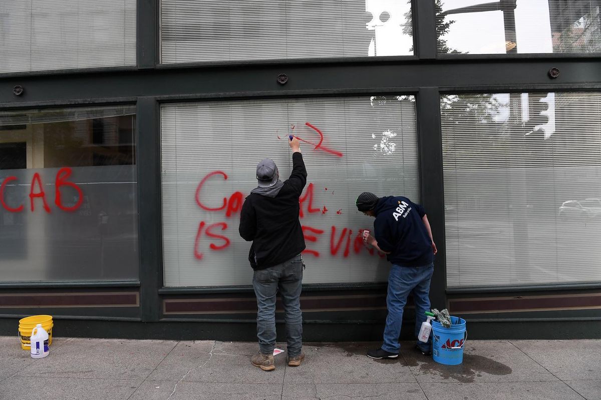 James White, left, and Kyle Larison , right, work to clean up graffiti on the Columbia bank building following Sunday night