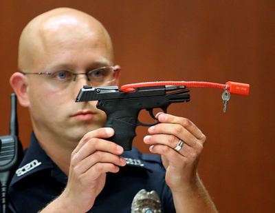 Sanford police officer Timothy Smith holds up the gun June 28, 2013, that was used to kill Trayvon Martin in Seminole circuit court in Sanford, Fla. The pistol George Zimmerman used in the fatal shooting of Martin is going up for auction online. (Joe Burbank / Associated Press)
