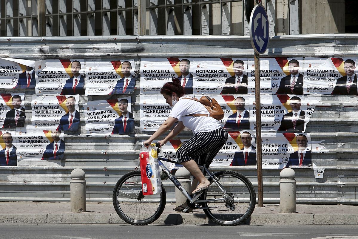 A woman rides a bicycle past electoral campaign posters of the largest opposition party VMRO-DPMNE set on a construction fence along a street in Skopje, North Macedonia on Saturday, July 11, 2020. North Macedonia holds its first parliamentary election under its new country name this week, with voters heading to the polls during an alarming spike of coronavirus cases in the small Balkan nation.  (Boris Grdanoski)