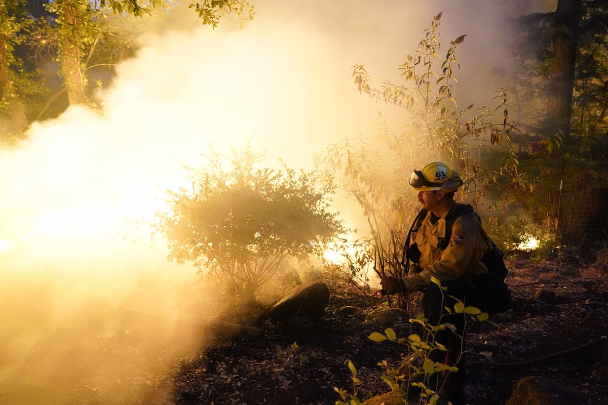 Firefighter Jeremy Damon of the Nevada Yuba Placer Fire Dept. monitors a controlled burn in the backyard of a home in front of the advancing CZU August Lightning Complex Fire Friday, Aug. 21, 2020, in Boulder Creek, Calif.  (Marcio Jose Sanchez)