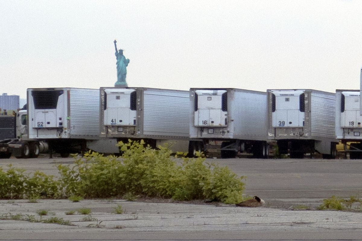 FILE — In this May 6, 2020 file photo, the Statue of Liberty is visible above refrigerator trucks intended for storing corpses that are staged in a lot at the 39th Street pier, in the Brooklyn borough of New York. New York City is still using refrigerated trucks to store bodies of coronavirus victims, more than a year after they were first set up as temporary morgues as deaths surged at at the height of the pandemic.  (Ted Shaffrey)