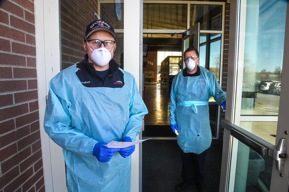 Spokane firefighters Jason Donahue, left, and Brad Bowers screen people entering the Spokane Fire Department Training Center where city and county officials declared an emergency due to COVID-19, Monday afternoon, March 16, 2020. (Dan Pelle / The Spokesman-Review)