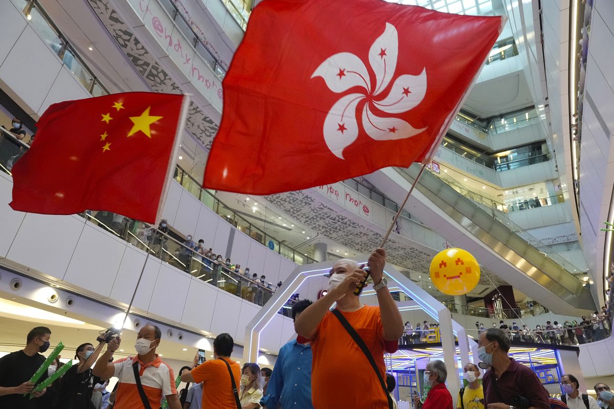 In this Friday, July 30, 2021 photo, people wave a Hong Kong flag and a Chinese national flag as they watch Olympics events at a shopping mall in Hong Kong. Hong Kong police arrested a man Friday, July 30, 2021, on suspicion of insulting the national anthem, after he was allegedly caught booing the Chinese national anthem and waving a Hong Kong colonial flag while watching an Olympic event at a mall.  (Vincent Yu)