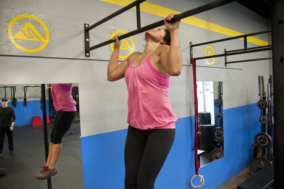 Encouraged by trainer Chris Benesch during a workout at CrossFit Spokane, Vanessa Branstetter fights her way up for another pullup. The day’s workout included a 400-meter run, 21 repetitions with a 35-pound kettle bell and 12 pull ups. The exercises were repeated three times. (Dan Pelle)