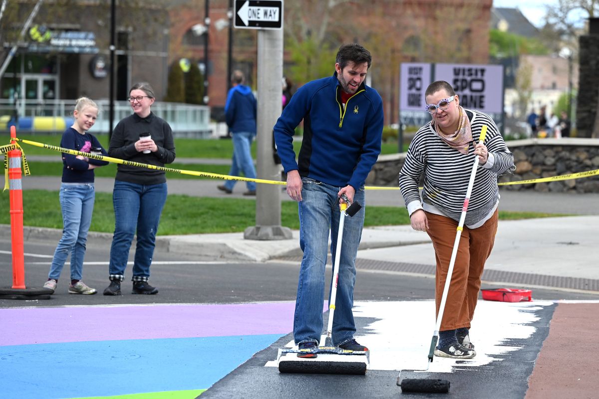 Spokane City Councilman Zack Zappone, left, and artist Tiffany Patterson paint the crosswalk at Howard Street and Spokane Falls Boulevard Sunday as part of a project to refresh the mural in time for the Expo ’74 anniversary, Bloomsday and the annual Pride celebration coming up in June. Behind, city Councilwoman Kitty Klitzke and daughter Violet Klitzke Eichstaedt watch the activities.  (Jesse Tinsley/THE SPOKESMAN-REVIEW)