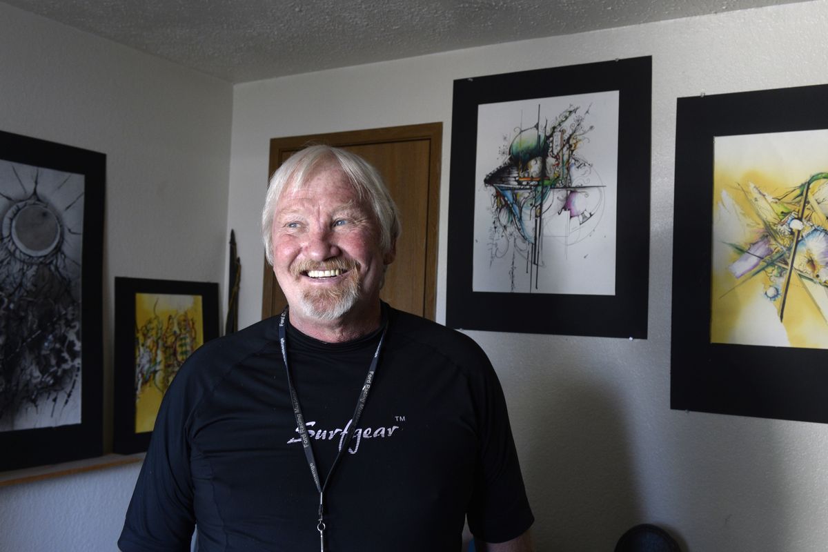 Brad Johnson, a school custodian by trade, stands with many of his works at his apartment in Spokane on Wednesday. He says his work is best described as abstract expressionism, though he hides motifs and representational imagery in his pieces. (Jesse Tinsley)