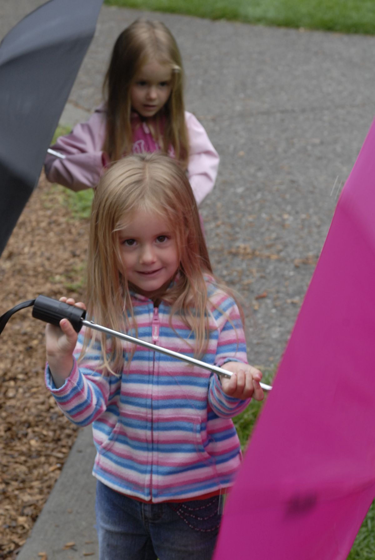 Sheltered from the rain, 3-year-old Paige Larson, front, and twin sister Elaina Larson play  at Manito Park. (Kate Clark / The Spokesman-Review)