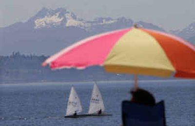 
A pair of sailboats floats past beachgoers at Seattle's Golden Gardens Park and in view of the Olympic Mountains Friday. 
 (Associated Press photos / The Spokesman-Review)