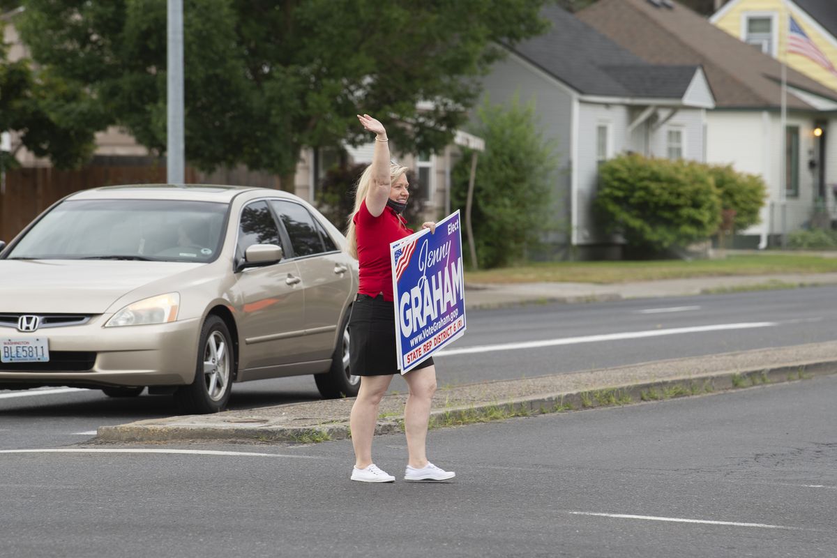 State Rep. Jenny Graham waves her campaign sign at the corner of Francis Avenue and Monroe Street, Thursday, July 23, 2020. With the COVID virus limiting personal contact with constituents, signs waving has taken on new importance.  (Jesse Tinsley/The Spokesman-Review)
