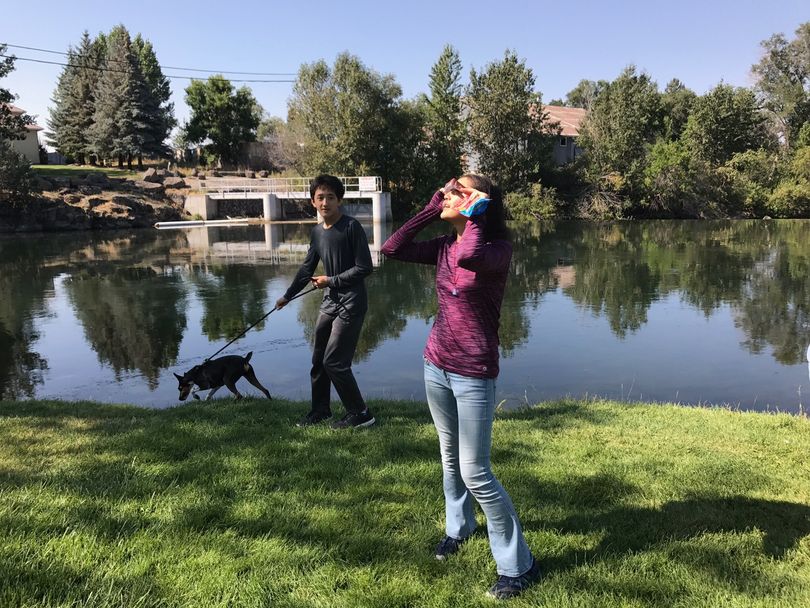 Sabrina Mueller, right, of Minneapolis, Minn., looks at the solar eclipse through eclipse glasses as her brother, Sebastian, holds their dog, Toby, at the St. Anthony Sandbar in St. Anthony, Idaho, on Monday, Aug. 21, 2017. (Betsy Z. Russell)