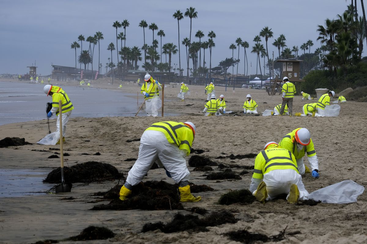 In this Oct. 7, 2021 photo, workers in protective suits clean the contaminated beach in Corona Del Mar after an oil spill in Newport Beach, Calif. A group of environmental organizations is demanding the Biden administration suspend and cancel oil and gas leases in federal waters off the California coast after a recent crude oil spill. The Center for Biological Diversity and about three dozen organizations sent a petition Wednesday, Oct. 20, 2021, to the Department of the Interior, arguing it has the authority to end these leases.  (Ringo H.W. Chiu)