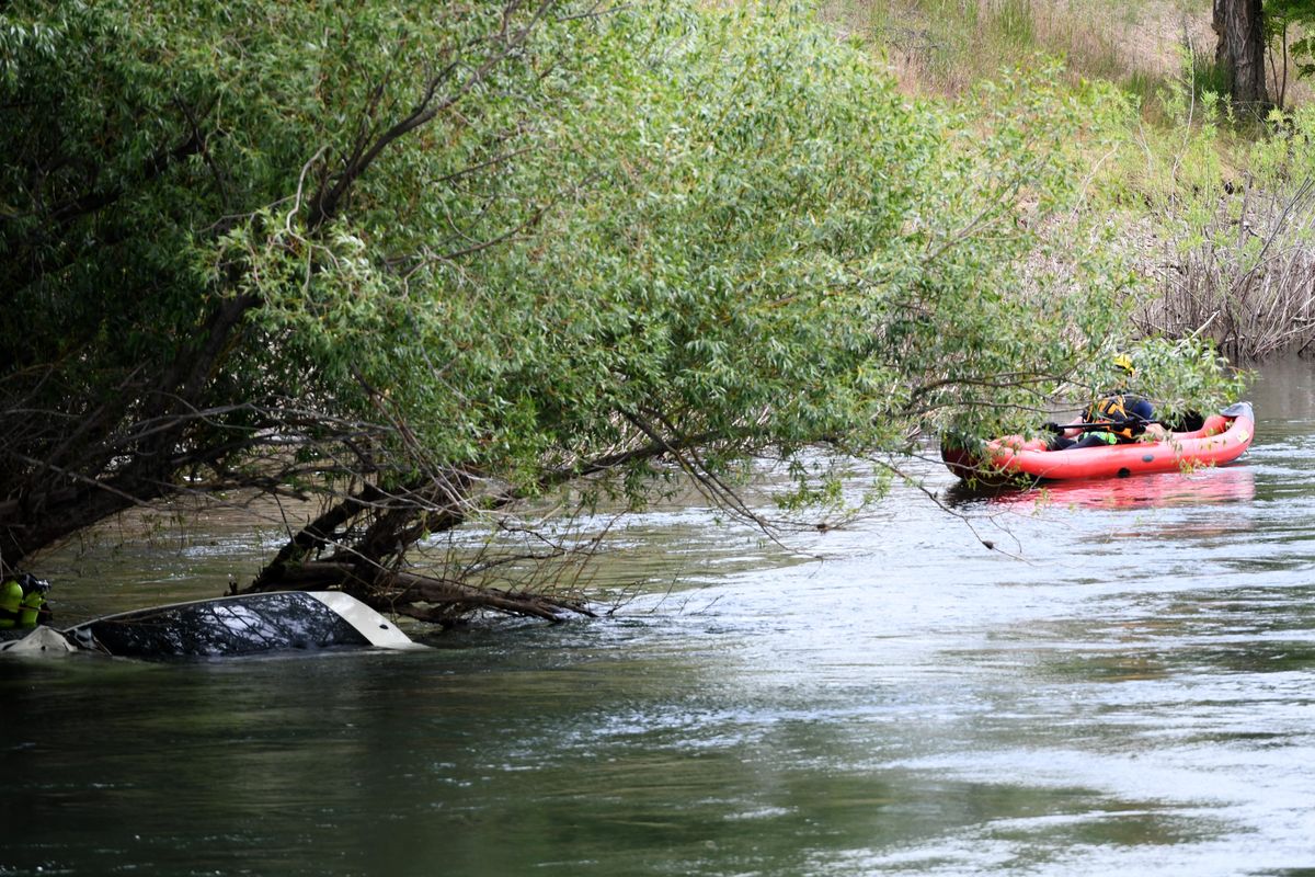 A water rescuer waits near the wreckage of a car that was caught in the branches of a riverside tree in the Spokane River near Sinto and Helena, close to the Mission Ave. bridge in east Spokane Friday, June 1, 2018. (Jesse Tinsley / The Spokesman-Review)