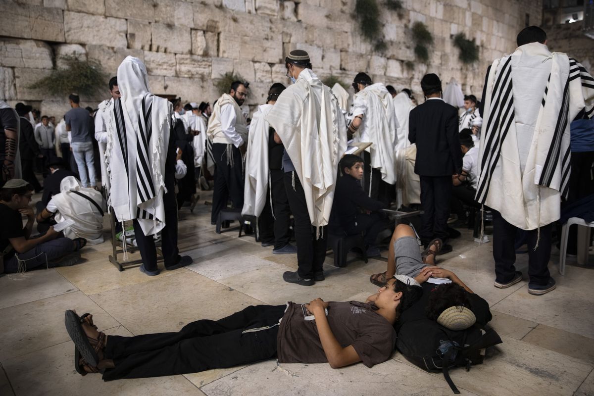 Ultra-Orthodox Jewish men pray as others are sleeping during the mourning ritual of Tisha B'Av (Ninth of Av) fasting and a memorial day, commemorating the destruction of ancient Jerusalem temples, at the Western Wall, the holiest site where Jews can pray in the Old City of Jerusalem, Sunday, July 18, 2021.  (Oded Balilty)