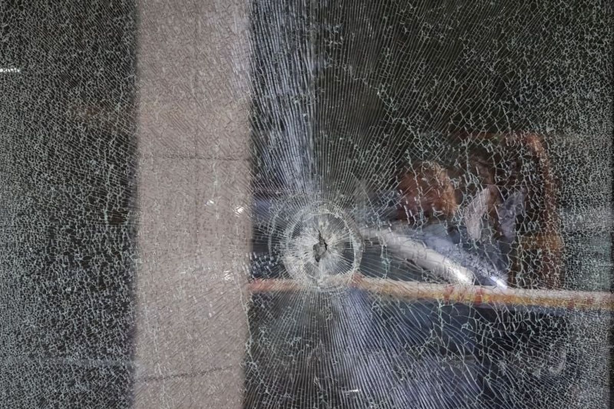 Residents reflected in the supermarket window with a bullet hole at the site of Saturday