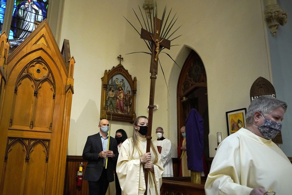 FILE - In this Sunday, March 28, 2021 file photo, altar server Samantha Holmes, of East Brookfield, Mass., center, carries a crucifix with palm leaves during a procession at the start of Palm Sunday Mass at Mary, Queen of the Rosary Parish in Spencer, Mass. For Christians across the United States, Easter services on Sunday will reflect an extra measure of joy as the nation experiences rising optimism after a year of pandemic. (Steven Senne)