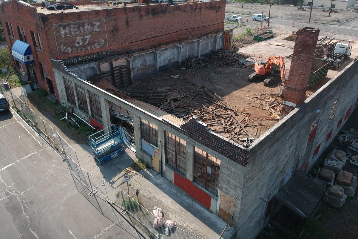 Crews take down the former garage, foreground, spanning a block from West Dean Avenue and West Cataldo Avenue that was built for an early bus line, then bought later by dairy business interests, on Friday, May 31, 2019. The old warehouse, at left, most recently a dance studio, in its early years was used as a horse stable associated with the dairy business which will also come down to make way for the future Sportsplex being planned by the Public Facilities District and Spokane Sports Commission. (Jesse Tinsley / The Spokesman-Review)