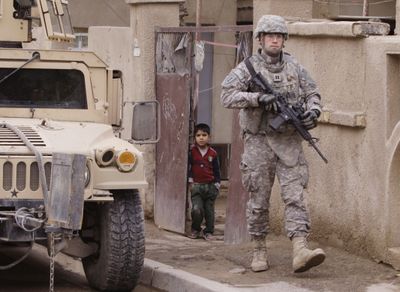 An Iraqi boy looks out of his gate at a U.S. soldier  on a routine patrol in Baghdad  on Tuesday.  (Associated Press / The Spokesman-Review)