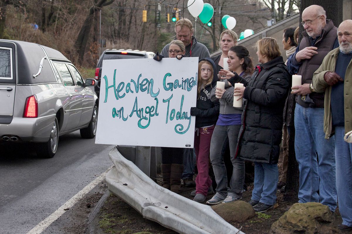 Friends and co-workers hold a sign as the hearse and funeral procession for James Mattioli, 6, who died in the Sandy Hook Elementary School shootings, approaches the St. John