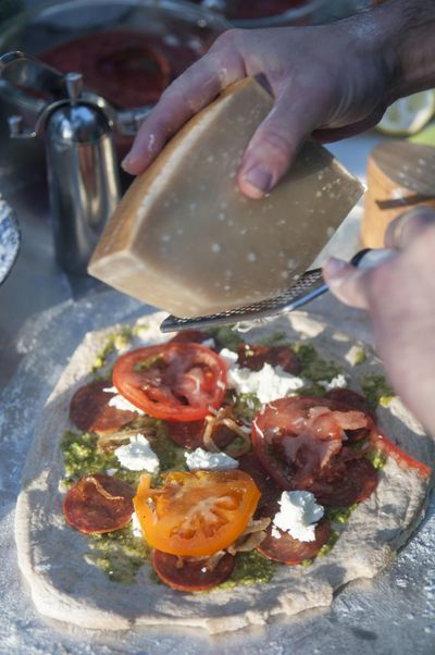 Shaun Thompson Duffy grates Parmigiano-Reggiano over top a pizza with goat cheese, tomatoes and pepperoni at a backyard pizza party in Port Falls in this file photo. (Adriana Janovich / The Spokesman-Review)