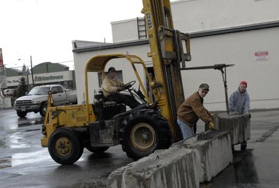 Spokane Valley Heritage Museum volunteers Herman Meier, front, and Dylan Arnette, in red hat, guide a concrete block into place as Tommy Dunagan of Neil’s Welding and Repair lowers it to on the museum’s property line April 13.  (J. BART RAYNIAK / The Spokesman-Review)