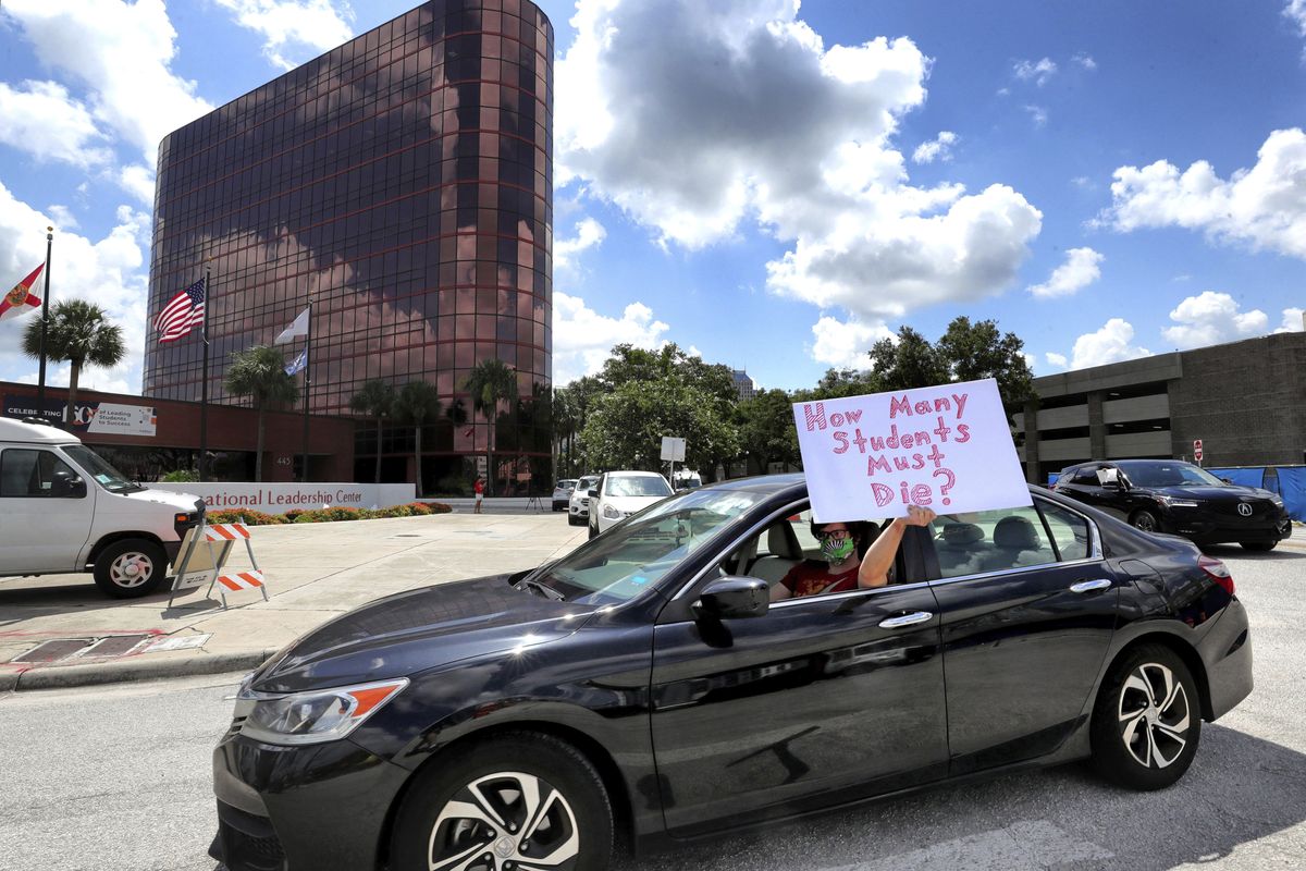 FILE - In this July 7, 2020, file photo, a teacher holds up a sign while driving by the Orange County Public Schools headquarters as educators protest in a car parade around the administration center in downtown Orlando, Fla. As the Trump administration pushes full steam ahead to force schools to resume in-person education, public health experts warn that a one-size-fits-all reopening could drive infection and death rates even higher.  (Joe Burbank)