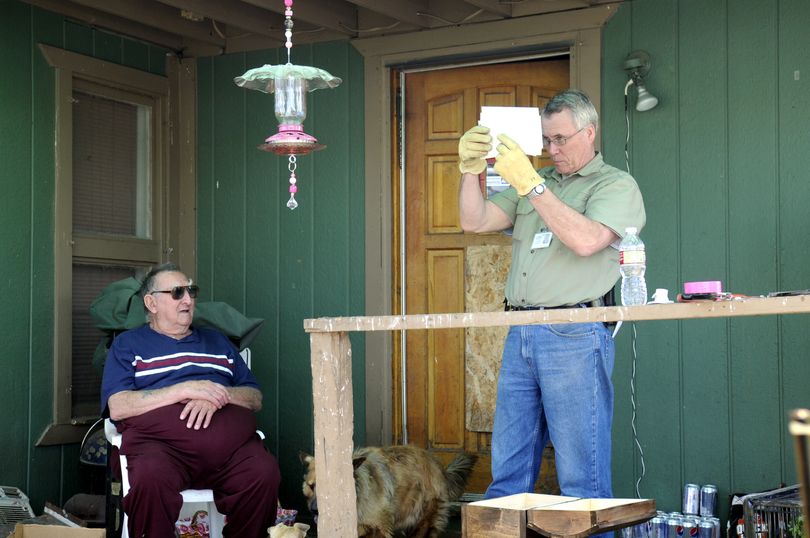 Spokane County Sheriff's Detective Dan Spivey goes through miscellaneous mail on the porch of Jim Rash, left, on Wednesday after Ricky Wayne Everett was arrested nearby. Everett lived at Rash’s home as a friend of his teenage grandson. Spivey and other investigators took most of Everett’s possessions as evidence, including mail. (Jesse Tinsley / The Spokesman-Review)