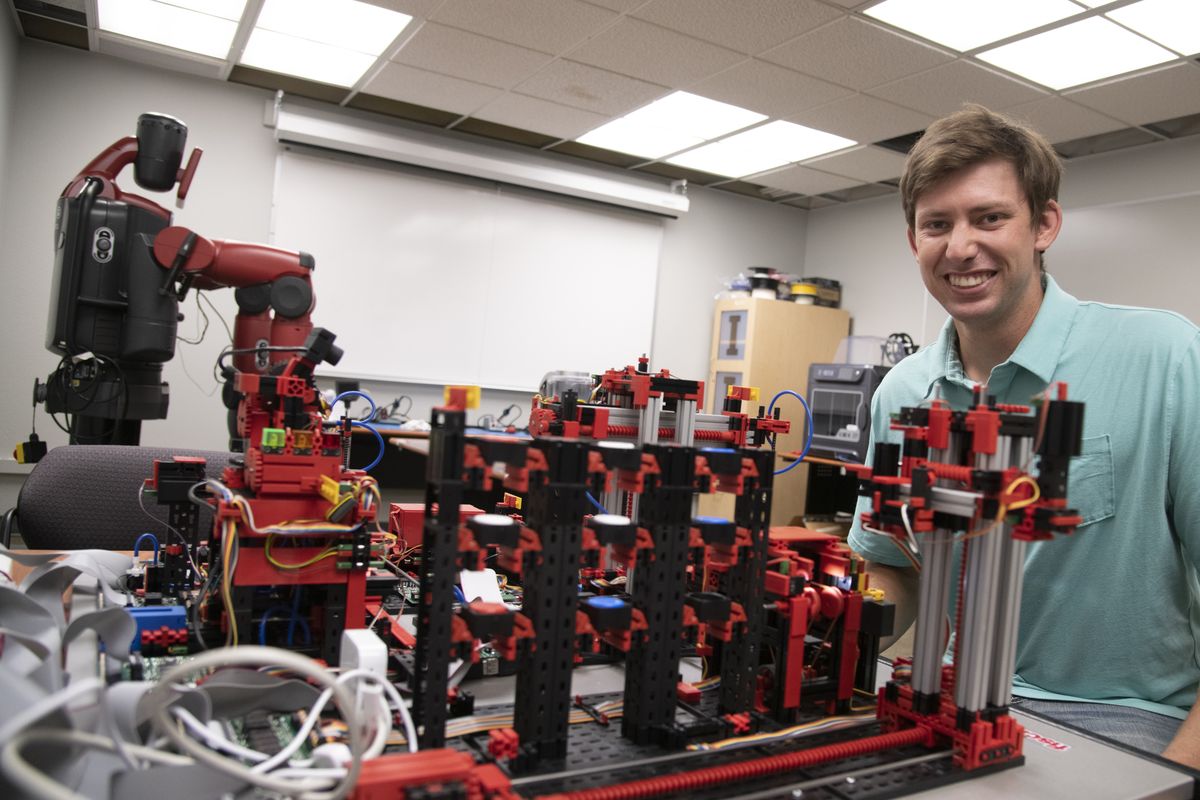 Robotics student Nathan Osterberg sits next to the tabletop model of an automated factory Tuesday, Aug. 31, 2021 used at North Idaho College in Coeur d’Alene, the new location of the University of Idaho robotics program that has been in Coeur d’Alene for three years. The Coeur d’Alene-based program offers advanced degrees in robotics, predominantly used in manufacturing.  (Jesse Tinsley/THE SPOKESMAN-REVI)