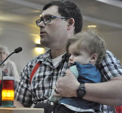 – 
Tim Moses, of Tumwater, Wash., holds his 1 year-old daughter Lily as he testifies in favor of a bill to require secure storage of firearms in the home. Moses said he can get to his locked firearms in four seconds and “if I need my gun faster than that, I wear it.” (Jim Camden / The Spokesman-Review)