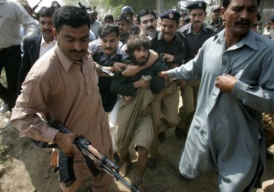 A Pakistani police officer arrests one of the alleged gunmen at the compound of a police training school on the outskirts of Lahore, Pakistan, on Monday after an attack that left about 20 dead.  (Associated Press / The Spokesman-Review)