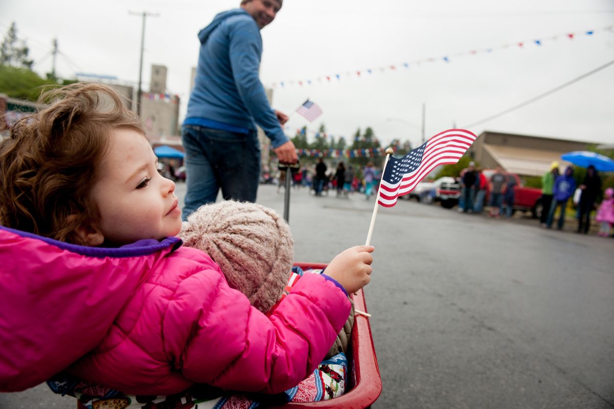 Hannah Konshuck, 3, waves a flag as her father, Evan, pulls her and her brother Eli, 1, in a wagon Saturday during Fairfield’s 2014 Flag Day children’s parade in Fairfield, Wash. (Tyler Tjomsland)