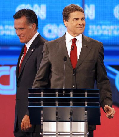 Former Massachusetts Gov. Mitt Romney, left, passes behind Texas Gov. Rick Perry during a break in the debate Monday. (Associated Press)