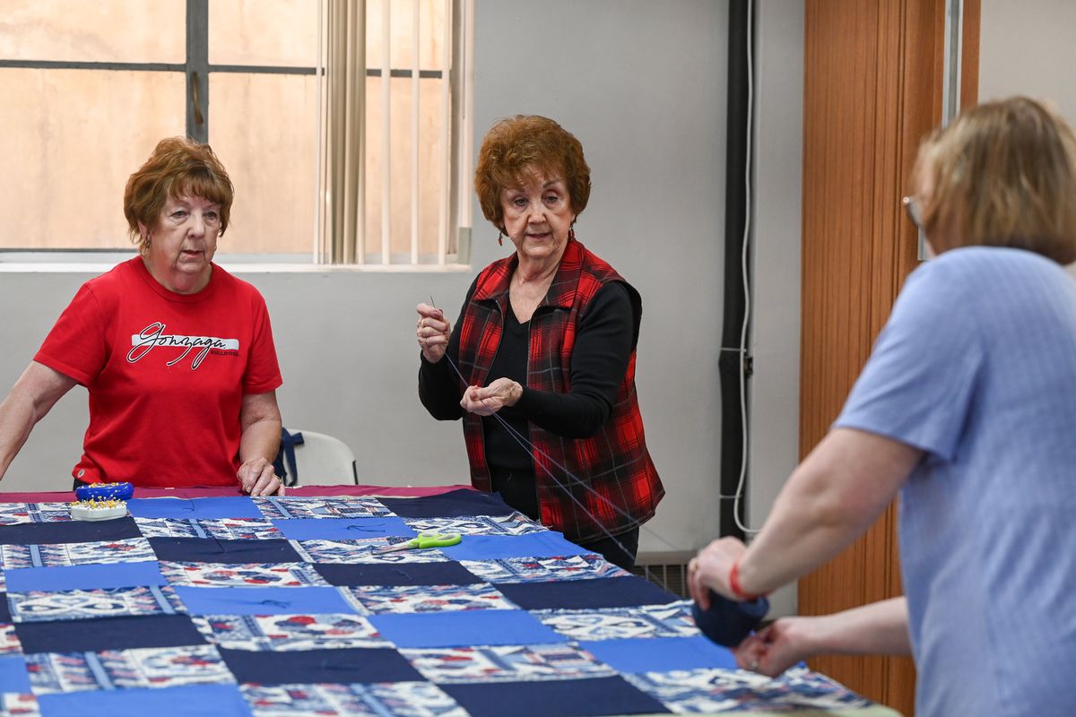 Sisters Barbara Hilbush, left, and Alice Kerr, center, measure out string for tying the layers of quilting together during a regular quilting session at Pilgrim Lutheran Church in north Spokane Wednesday, April 24, 2024. The group, which dates back many years, makes dozens of quilts a year for World Relief, Quilts of Valor and other ways in which quilts are given away.  (Jesse Tinsley/The Spokesman-Review)