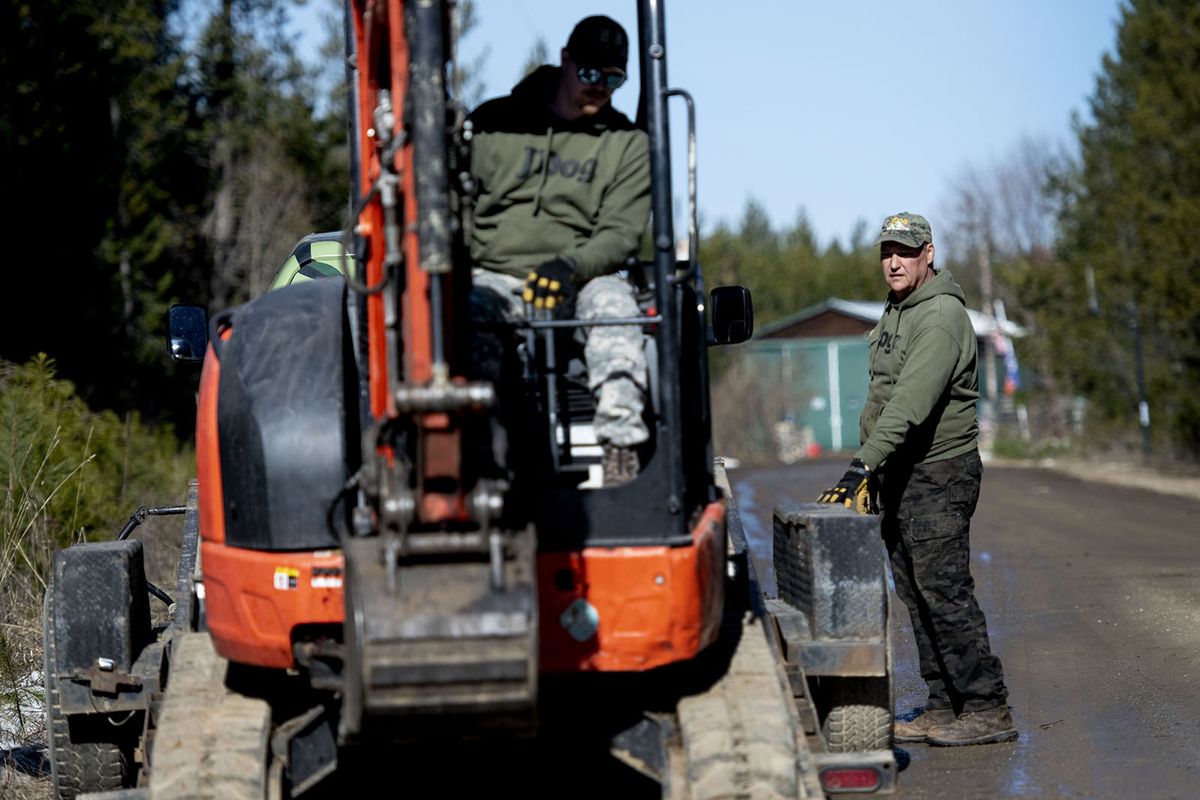 John Merwald, right watches as one of his employees onloads a backhoe at a property in Athol on Wednesday, March 17, 2021. He served the country for a decade in the Marine Corps and now is serving the community through his business, JDog Junk Removal & Hauling North Idaho. JDog is a franchise that employs veterans, military and their families.  (Kathy Plonka/The Spokesman-Review)