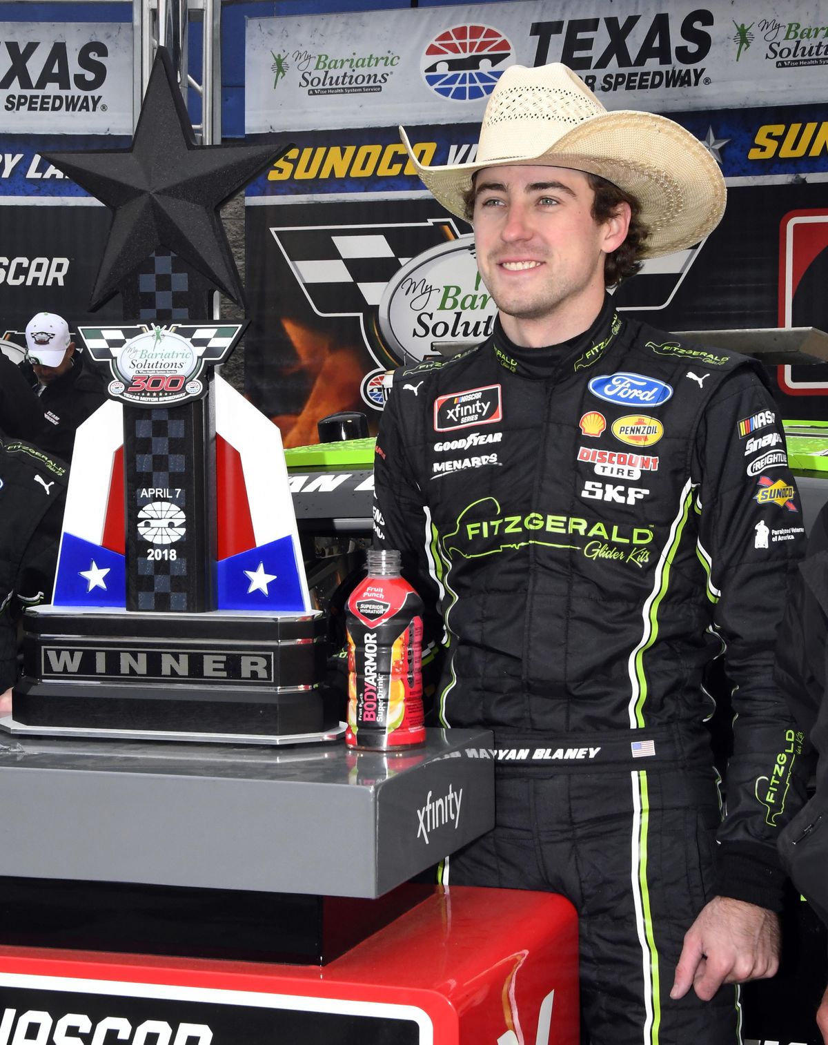 Ryan Blaney poses for photos by the trophy in Victory Lane after winning a NASCAR XFinity series auto race in Fort Worth, Texas, Saturday, April 7, 2018. (Larry Papke / Associated Press)