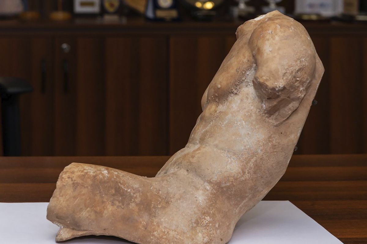 In this Friday, March 19, 2021, photo provided by the Greek Police shows a 5th century B.C. statue about 14.5 inches, depicting a seated young man who slightly reclines. Greek police say a man has been arrested on suspicion of antiquities smuggling for trying to sell an ancient marble statue of "exceptional artwork and significant archaeological value" that once likely adorned the pediment of a building on Athens