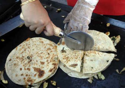 
Vinita Yemul cuts fresh quesadillas into sections for customers at the Kootenai County Farmers' Market in Coeur d'Alene. Yemul's boss, Harlow Morgan, runs a quesadilla stand there, and her standard recipe is a pair of tortillas filled with cheese and fried onions, cabbage, zucchini and spinach. 
 (Jesse Tinsley / The Spokesman-Review)