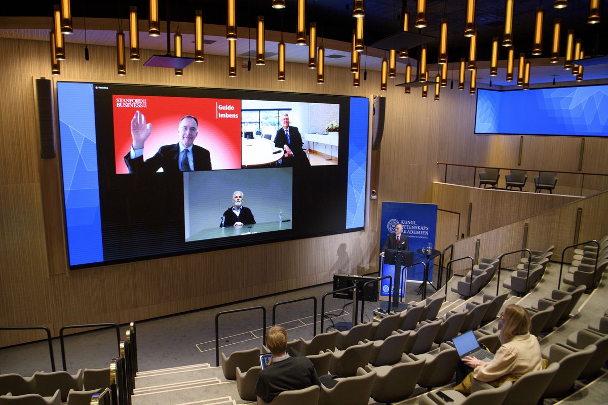 Nobel laureates Guido W Imbens (economic sciences) top left, David W C MacMillan (chemistry), top right, and Klaus Hasselmann (physics), appear on screen and Secretary General of the Royal Swedish Academy of Sciences Goran K Hansson, bottom right, speaks during a digital press conference at the General of the Royal Swedish Academy of Sciences in Stockholm, Monday, Dec. 6, 2021.  (Jessica Gow)