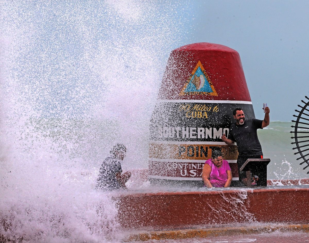 FILE- Key West resident Pedro Lara takes a selfie in front of the Southernmost Point as waves from Hurricane Irma crash over the wall on Sept. 9, 2017. The 20-ton concrete buoy, which marks the Southernmost Point and 90 miles to Cuba, is one of Key West’s famous landmarks. Tourists flock to the marker every day to take photos, snap selfies, buy a souvenir or two.  (Charles Trainor Jr)