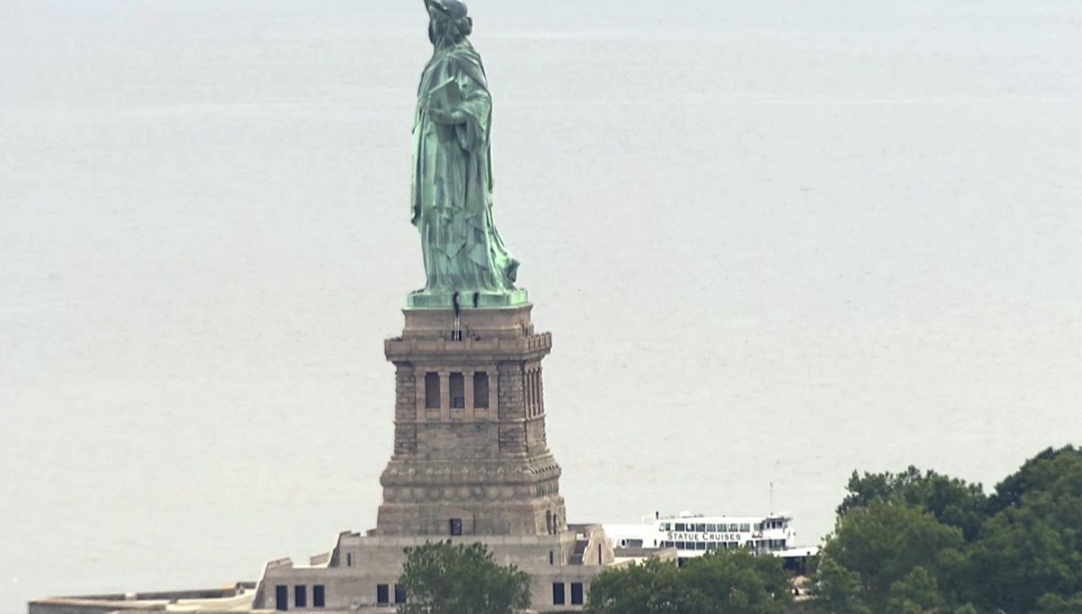 This image taken from video shows people climbing on the side of the Statue of Liberty