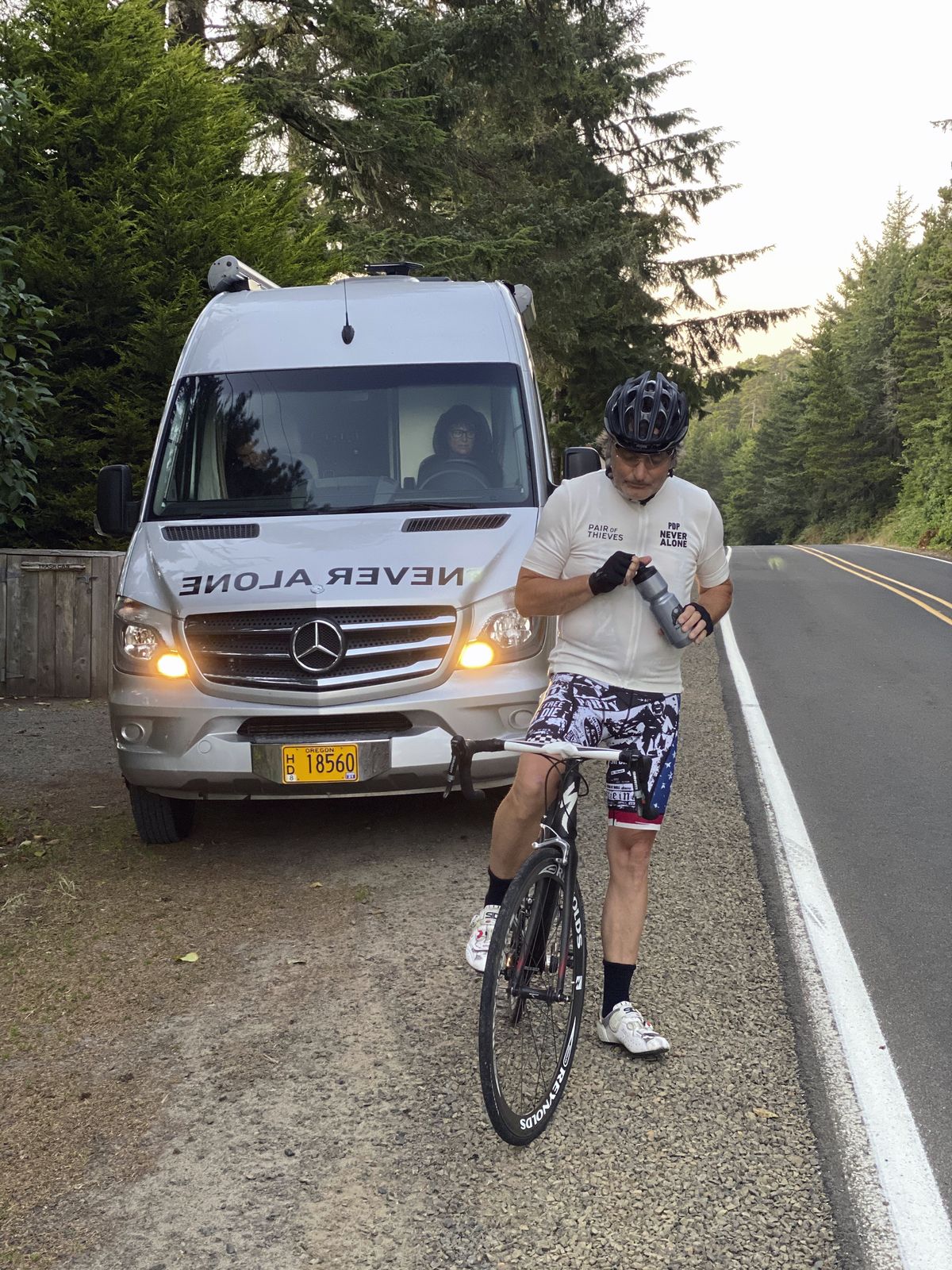 This photo provided by Pair of Thieves shows Doug Peterson stopped alongside the road with his wife, Lori, driving the support van as he cycles from the Canadian border to the Mexican border, last week in Pacific City, Ore.  (Alan Stuart)