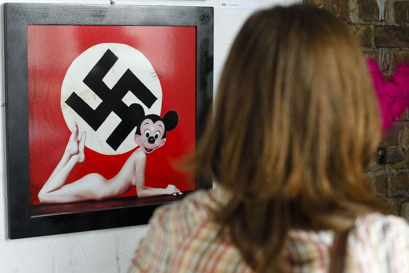 A woman stands in front of a artwork by Italian artist Max Papeschi at the exhibition 'Abnormal Nudes' at the alternative art house Tacheles in Berlin on Tuesday, July 13, 2010. The  art poster hung on a Polish street that blends Mickey Mouse's innocent image with that of a swastika and a nude woman's body is causing a stir in Poland, where memories of suffering inflicted by Nazi Germany remain strong.  The poster, which went up last month in the western city of Poznan just steps from an old synagogue, is an Italian artist's critical take on what he calls the 