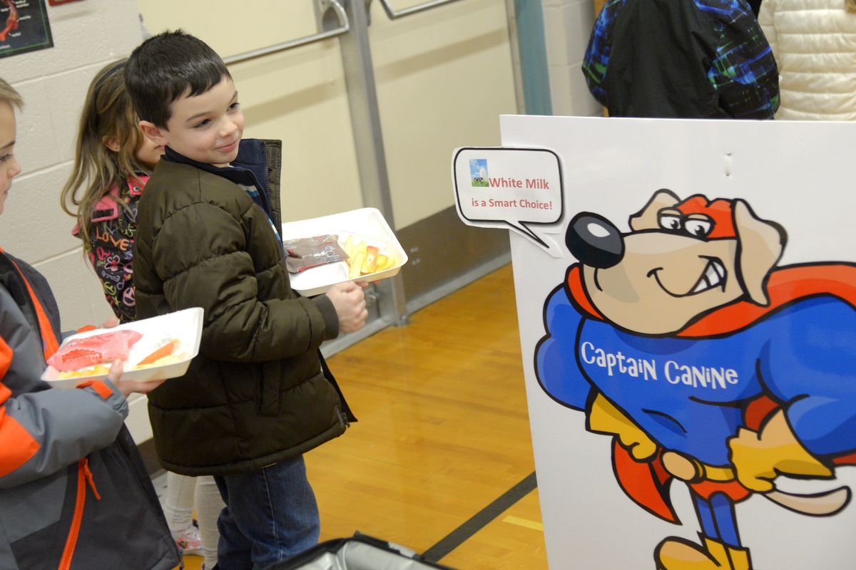 Solomon Toft, left and Evan Lucky, both first-graders at Summit School, pause to look at a poster of Captain Canine, a mascot that Central Valley School District is using to make suggestions to students going through the lunch line, on Monday. (Jesse Tinsley)