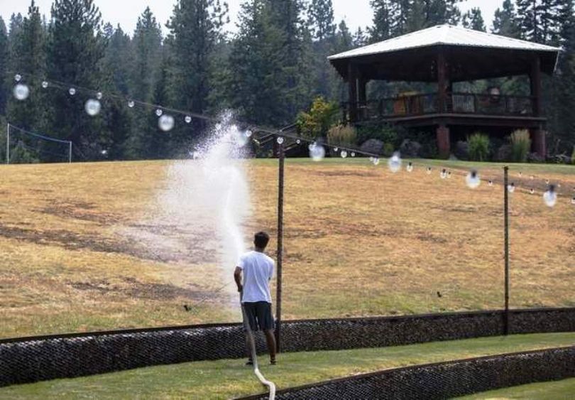 Settlers Creek employee Dylan Vahey sprays water on a grass burn spot near the property's amphitheatre Monday afternoon. Last week's fire destroyed the barn and a westerly wind blew sparks into nearby pastures and forest land. (Loren Benoit/Press photo)